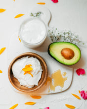 Load image into Gallery viewer, The Hydrating Hair Mask and ingredients artfully staged with a wooden bowl of the product, an avocado and sunflower petals